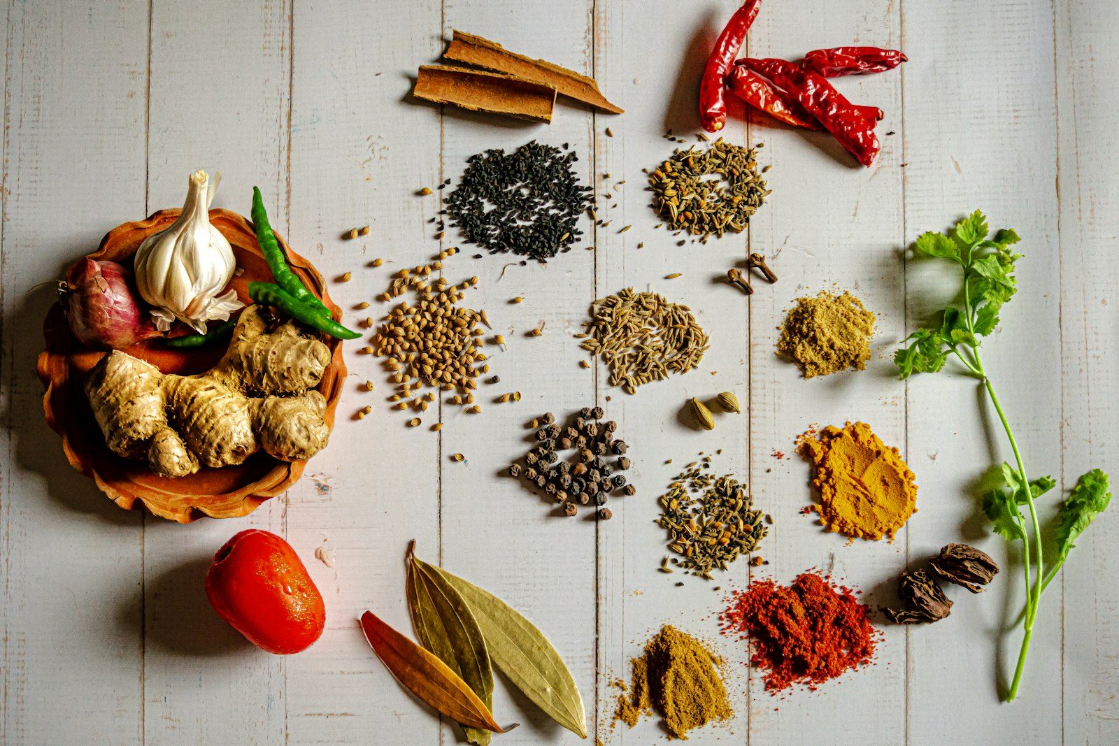 Flatlay rempah-rempah pilihan — cabai kering, bawang, kemiri, dan lada di atas meja kayu putih
